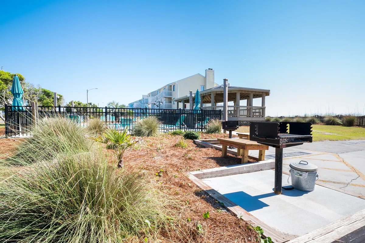 An outdoor grill area complete with a picnic table, pool area in the background, and landscaped greenery, creating a relaxed and communal atmosphere for gatherings and cookouts.