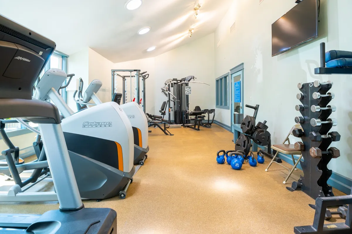A well-equipped fitness room featuring treadmills, weight machines, a dumbbell rack, and various fitness equipment, all in a motivational, clean setting.