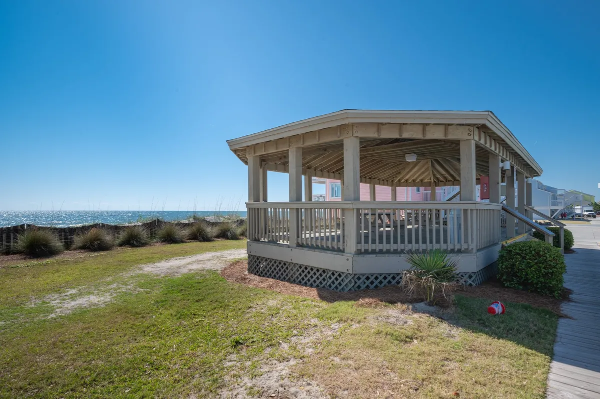 A charming pavilion structure sits on a lush grassy area overlooking the ocean. The open design invites couples to relax, enjoy a picnic, or sip morning coffee with uninterrupted sea views. The atmosphere is inviting and serene, blending natural beauty with a sense of shared experience.