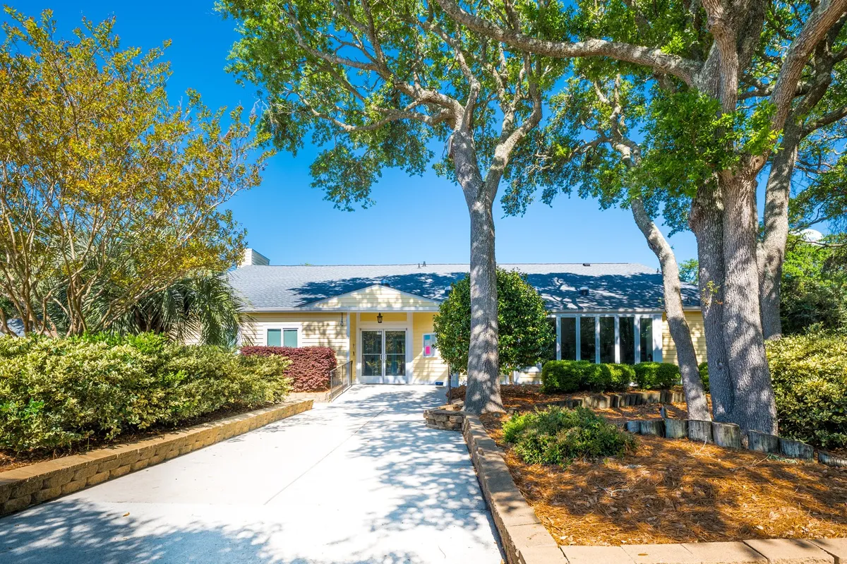 The main entrance of the property framed by large trees and beautifully landscaped gardens. The inviting path and outdoor seating suggest a welcoming environment ideal for gathering with friends and enjoying the fresh air.