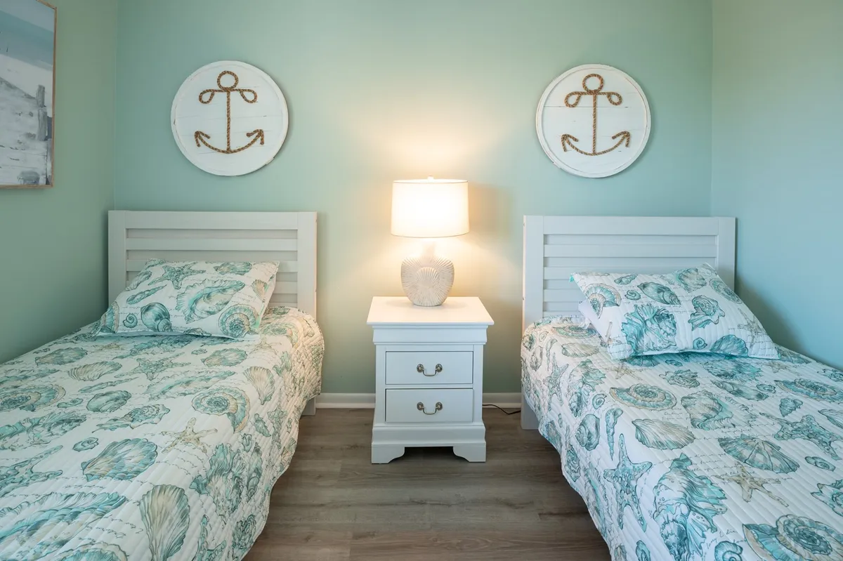 The second bedroom is shown with two cheerful twin beds, a bedside table with a lamp for nighttime reading, and playful wall art. Sunlight streams through the windows, creating a light-hearted and welcoming atmosphere ideal for families or friends traveling together.