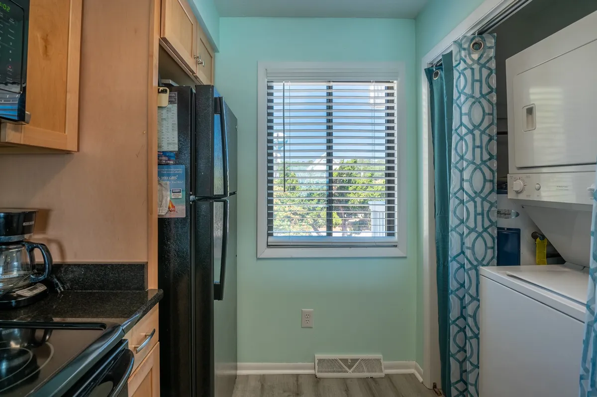This interior shot focuses on the kitchen, highlighting modern appliances, a window with blinds, and a laundry area set conveniently within the space. The layout showcases the practicality and design of the area, confirming the full kitchen and in-unit washer/dryer amenities.